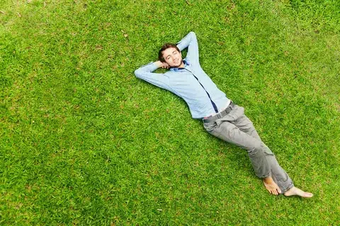 Happy relaxed man lying on green grass