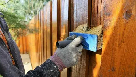 worker staining fence with brush