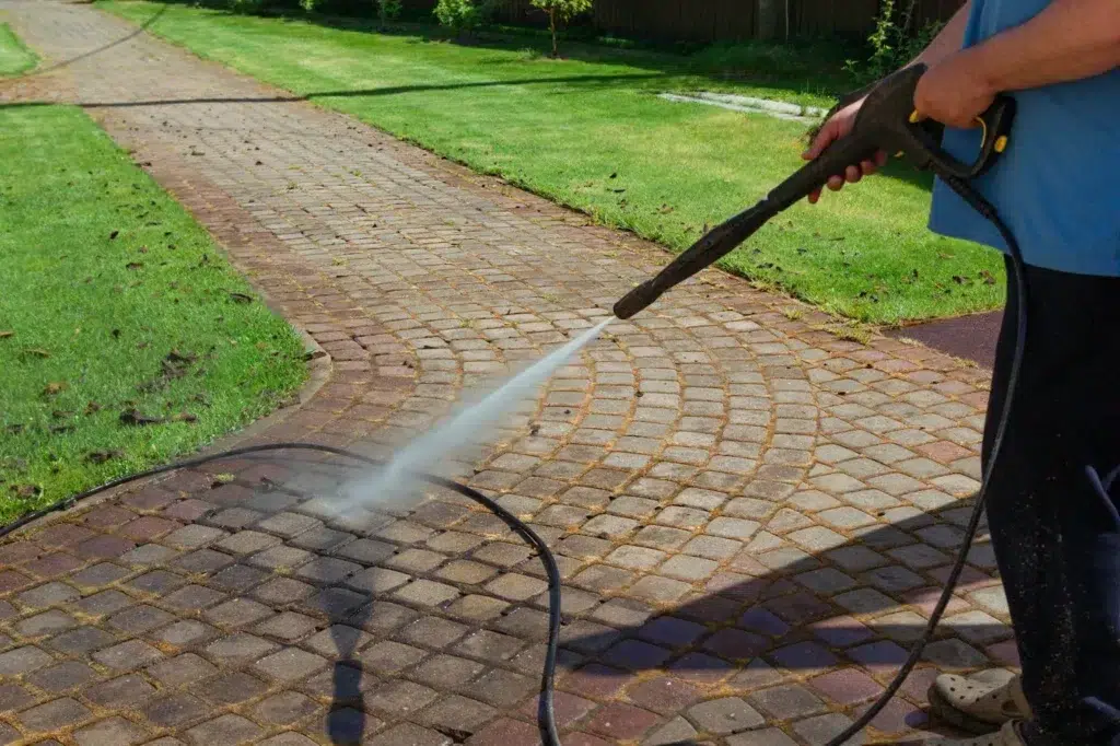 Worker power washing residential garden path in a yard
